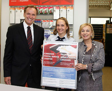 The Honourable Rob Merrifield, Minister of State (Transport), left, Canada Post employee Jennifer Tickstra, centre and Canada Post President and Chief Executive Officer, Moya Greene at right at an event to announce the new Canadian Postal Service Charter at the Ilderton, Ontario Post Office.
